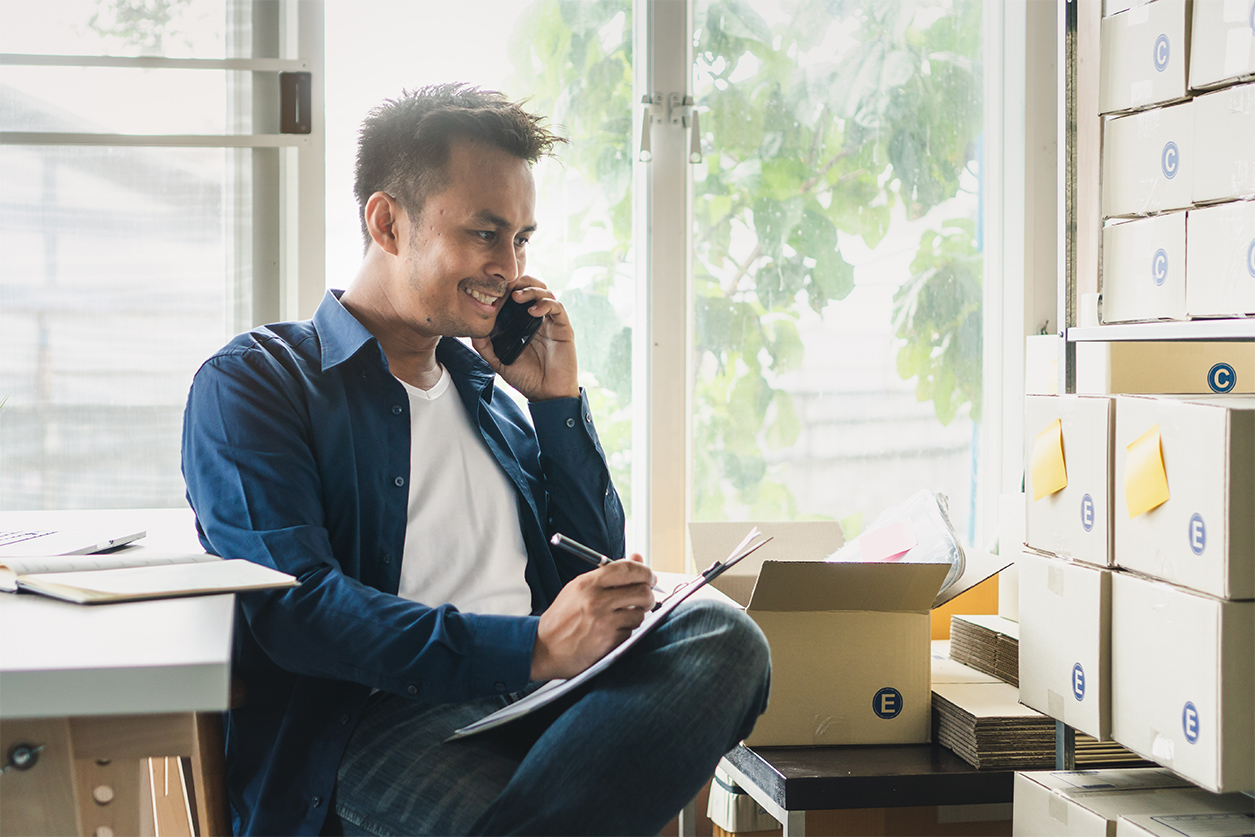 Male e-commerce business owner taking notes in the office space he obtained using a business loan.