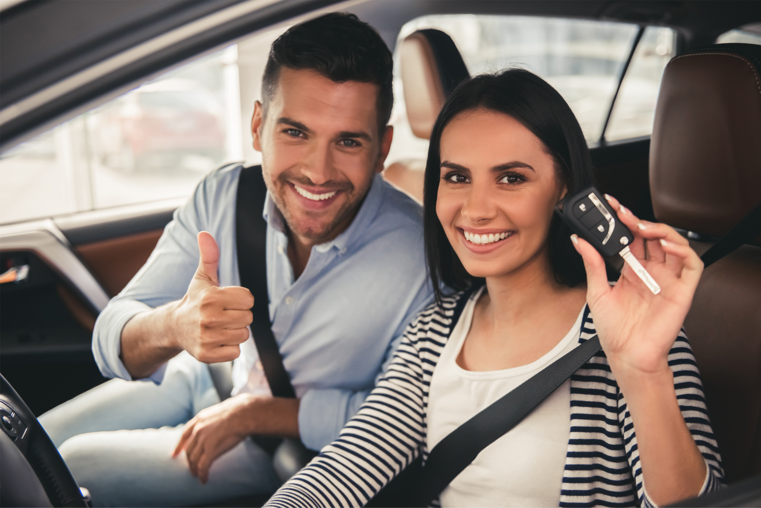 A happy couple is sitting inside their car holding up the key after financing with a used auto loan.