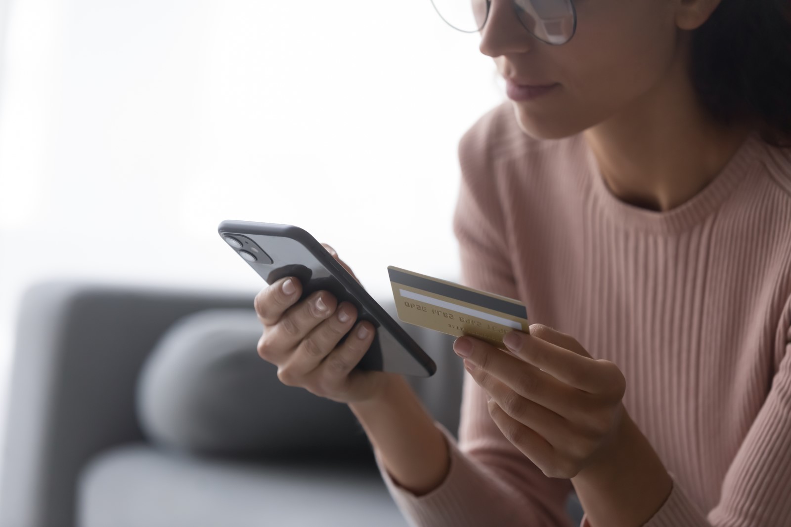 Close up of a young woman holding a smartphone and credit card to make an online purchase